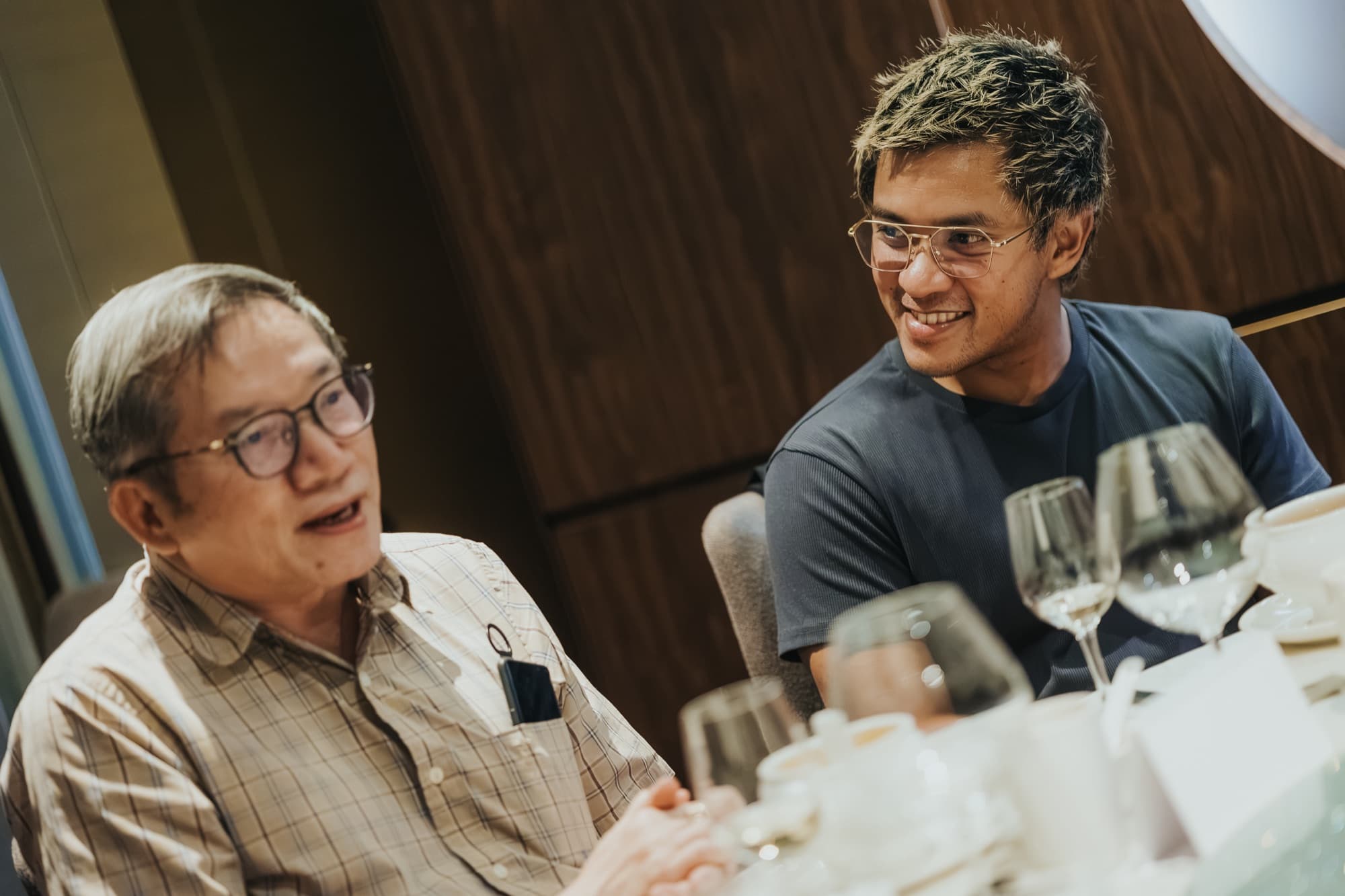 Two roundtable participants in conversation at the table, one speaking while the other listens and smiles.